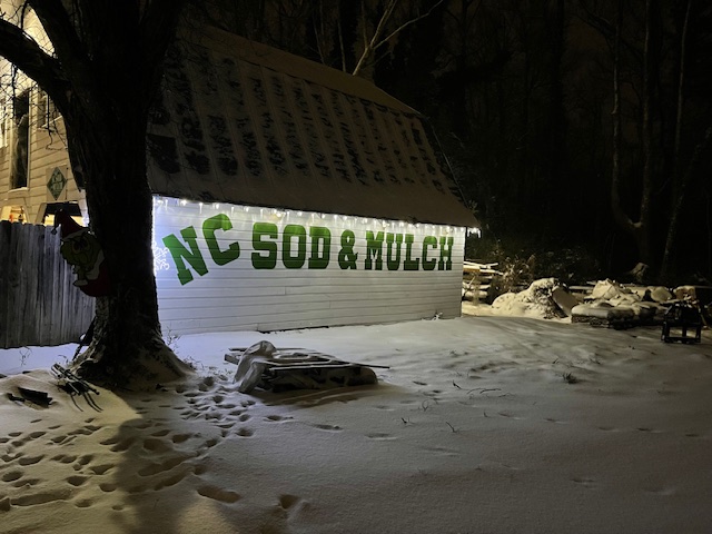 A gambrel style barn lit up with lights in the snow.